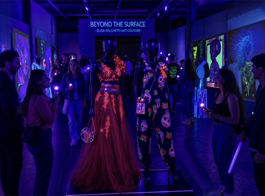Visitors in a UV-lit gallery with glowing paintings and garments
